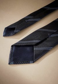 Cravatta blu navy realizzata in tessuto testurizzato con un motivo sottile, caratterizzata da strisce diagonali azzurre e una punta appuntita.