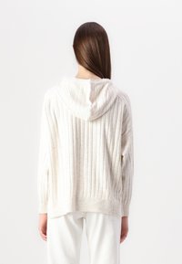 Cremefarbener Kapuzenpullover mit vertikalen Rippungen, langen Ärmeln und lockerer Passform. Weiche Textur, mit einem gerippten Saum abgeschlossen.