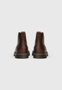 Botas de tobillo de cuero marrón con superficie texturizada, puntera redonda y suela de goma negra, con un ligero tacón y una tirador en la parte posterior.
