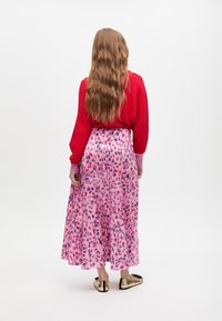 Dlouhá růžová sukně s leopardím vzorem, doplněná jasně červeným topem. Tento outfit se vyznačuje splývavou látkou a metalickými zlatými balerínami.