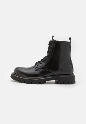 Bottes cheville en cuir noir avec un bout arrondi, une fermeture à lacets, une languette de tirage et une semelle robuste à rainures horizontales pour une meilleure traction.