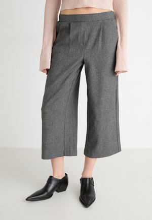 Gray, wide-leg trousers with pleats, made from a textured fabric. Paired with black, pointed-toe ankle boots featuring a buckle detail.