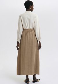 Lys creme langærmet bluse med krave, parret med en svævende, ankellang brun nederdel og sorte flade sandaler.