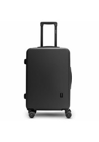 Maleta rígida negra de forma rectangular, con mango retráctil y cuatro ruedas para facilitar el movimiento. Presenta una superficie texturizada y un detalle de logo.