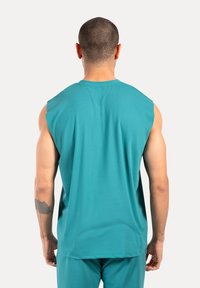 Ärmelloses türkisfarbenes Oberteil aus glattem Stoff, mit einem runden Ausschnitt und lockerer Passform, einem dezenten Glanz und ohne sichtbare Muster.