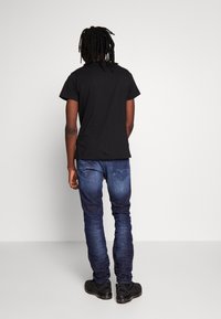 Svart bomulls t-shirt med korta ärmar, tillsammans med mörkblå jeans med bakfickor och en gradvis färgövergång. Svarta sportskor.