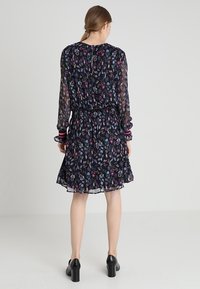 Svart blommig klänning med långa, genomskinliga ärmar, elastisk midja och en utfälld kjol. Har flerfärgade blommönster och randiga manschetter.