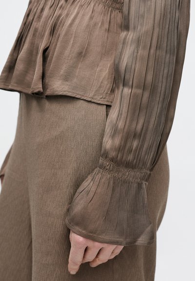 Barna réteges felső pliszírozott hosszú ujjakkal és fodros szegéllyel, semleges tónusú, ugyanolyan textúrájú szoknyával párosítva.