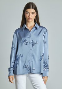 Camicia azzurra in raso con bottoni e maniche lunghe, caratterizzata da ricami floreali in paillettes. Texture liscia e vestibilità comoda.