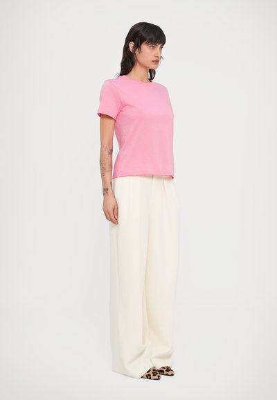 Ροζ κοντομάνικο μπλουζάκι σε συνδυασμό με μπεζ παντελόνια φαρδιάς γραμμής. Το υποδήματα έχουν σχέδιο με λεοπάρ. Ομαλή υφή υφάσματος σε όλο το σύνολο.