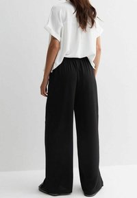 Pantalons larges noirs avec une taille élastique, fabriqués en tissu léger. Associés à un haut blanc à manches courtes ample.