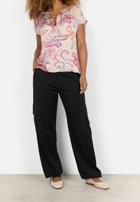 Blouse à manches courtes, de couleur claire, avec un motif cachemire et un col en V, associée à un pantalon cargo large et noir avec des poches latérales.