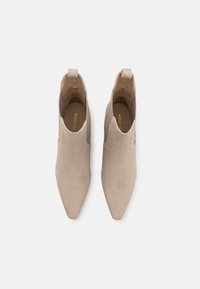 Paire de bottines beige en daim à bout pointu avec languettes de tirage, vues de dessus sur fond blanc.