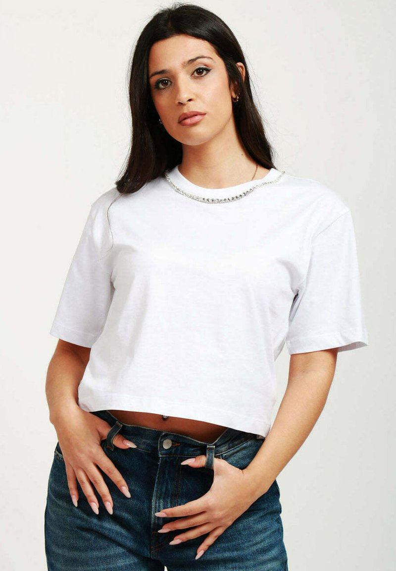 T-shirt bianco corto con maniche corte, dotato di collare decorativo in strass, abbinato a jeans in denim a vita alta.