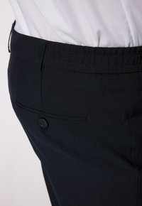 Dunkelblaue Hose aus strukturiertem Stoff, mit einer Gesäßtasche mit Knopfverschluss und einem glatten Bund. Schlichtes Design, taillierte Passform.