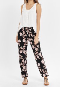 Top bianco senza maniche con dettagli di bottoni abbinato a pantaloni neri con stampa floreale che presenta fiori rosa e bianchi, vestibilità ampia e vita con cordoncino.