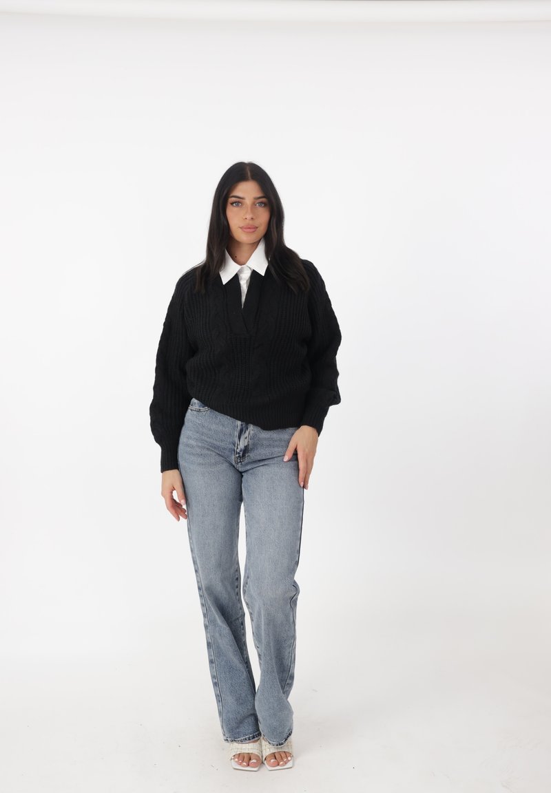 Maglione nero a trecce con scollo a V, abbinato a jeans azzurri a vita alta e tacchi bianchi aperti. Camicia bianca solida con colletto sotto.