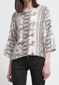 Blommönstrad, krämfärgad topp med svarta geometriska detaljer, lös passform och 3/4 ärmar. Matchad med svarta byxor, ser tyget mjukt och texturerat ut.