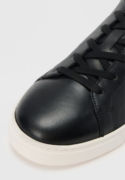 Čierna kožená teniska s okrúhlou špičkou, vybavená čiernymi šnúrkami, textúrovaným vrškom a bielou gumovou podrážkou. Detailný záber na oblasť špičky.