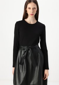 Top negro de manga larga combinado con una falda de cuero sintético negro que presenta un detalle de cintura anudada. Textura suave y silueta elegante.