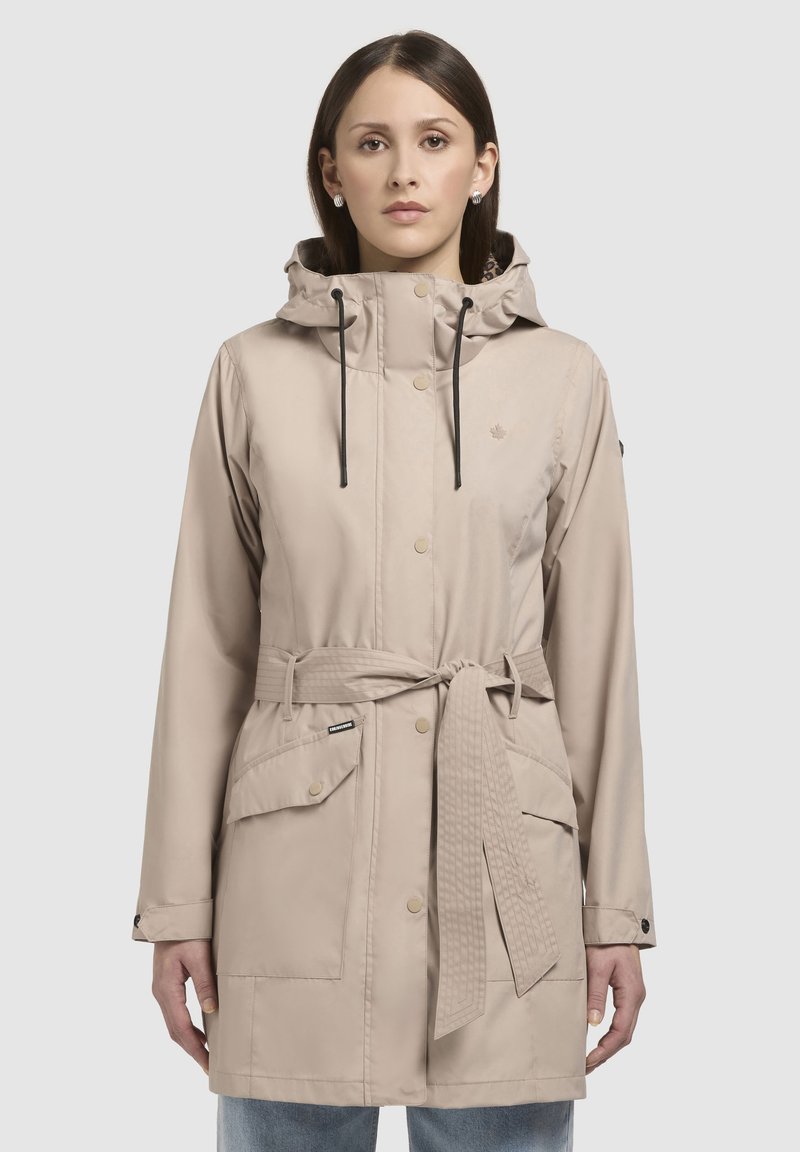 Beige waterdichte jack met een capuchon, knopen aan de voorkant, trekkoorden, zijzakken en een ceintuur in de taille. Gladde textuur met een klassiek ontwerp.
