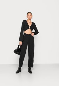 Top cropped preto de mangas longas com detalhe torcido na frente e recorte circular, combinado com calças pretas de cintura alta e botins pretos de salto.