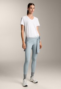 Bela v-majna majica, svetlo modre visoke leggings, svetlo modra zveza na vrhu, sivi gležnjarji, bele športne čevlje. Gladke teksture tkanin.