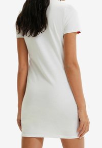 Bílá bavlněná šaty s krátkými rukávy, přiléhavý silueta a jemné květinové akcenty viditelné na manžetách rukávů. Hladká textura, délka po kolena.