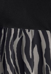 Schwarzer gerippter Oberteil, der in einen fließenden Rock mit einem grauen und schwarzen Zebramuster übergeht, aus einem weichen Stoff mit glatter Textur.