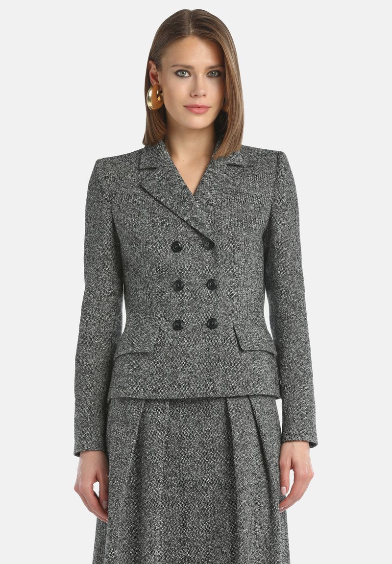 Veste double boutonnage en tweed gris avec un col cranté, des boutons noirs, et une coupe ajustée, au toucher lisse et à la forme structurée.