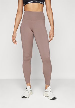 Leggings taille haute, ajustés, dans une couleur mauve atténuée. Fabriqués en matériau extensible avec des coutures et une texture lisse. Stylisés avec un soutien-gorge de sport noir.