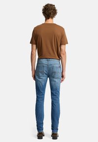 Jeans blu con una vestibilità affusolata, effetto sbiadito e tasche posteriori distintive. Abbinati a una maglietta a maniche corte marrone e scarpe scure.
