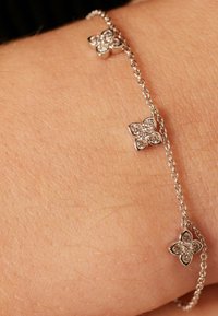 Bracelet en argent avec trois charms en forme de fleur, ornés de pierres claires regroupées. Le design de la chaîne est fin et délicat, mettant en valeur les charms.
