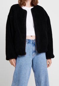 Sort fleece bomberjakke med rund hals, lynlås foran og oversized pasform. Sammen med lyseblå højtaljede jeans.