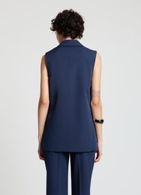 Veste sans manches bleu marine avec col, en tissu lisse. Présente une coupe ajustée et une coupe droite, associée à un pantalon assorti.