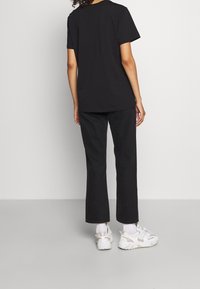 Camiseta de algodón negra con mangas cortas, combinada con pantalones negros y zapatillas ligeras. El conjunto es casual y tiene un ajuste relajado.