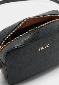 Černá texturovaná kabelka se zlatým zipem a logem LIUJO. Interiér je podšitý hnědou tkaninou a má obdélníkový tvar.