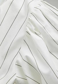 Țesătură albă cu dungi verticale negre subțiri, având textură adunată pe o parte și suprafață netedă. Vedere de aproape care arată detalii fine ale materialului.