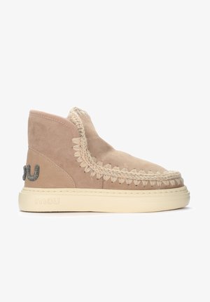 Stivale alla caviglia in suede color cammello con cuciture decorative e dettagli intrecciati. Presenta un logo testurizzato e una suola in gomma colore crema per un contrasto elegante.