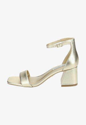 Sandali con tacco dorati metallici, con punta quadrata, sottile cinturino alla caviglia e un ampio tacco a blocco. Texture liscia e design minimalista.