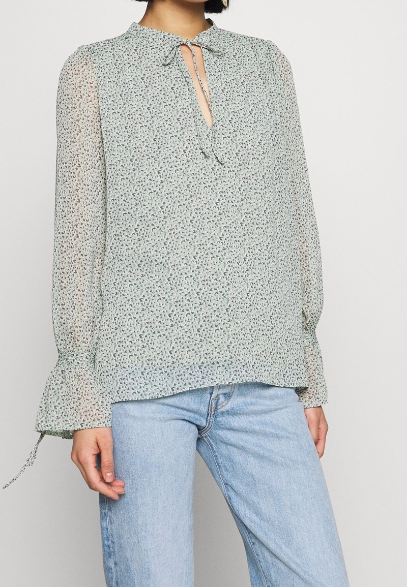 Ljusgrön blus med blommönster, nyckelhålsknut, långa genomskinliga ärmar med rynkade manschetter och en lös passform.