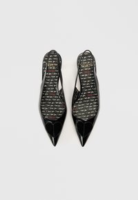 Sapatos slingback em couro envernizado preto com bicos pontiagudos, detalhes em forma de coração e uma palmilha estampada com o texto "Amo-te" em várias cores.