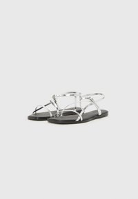 Sølv flate sandaler med tynne stropper og et enkelt design. Sålen er svart, noe som gir kontrast til den metalliske overdelen.