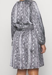 Robe en imprimé serpent noir et blanc avec des manches longues, un waistband élastique, un encolure cintrée et un ourlet évasé. Texture de tissu lisse.