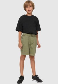 T-shirt en coton noir associé à un short vert kaki avec une taille élastique, terminé par des baskets de sport noires.