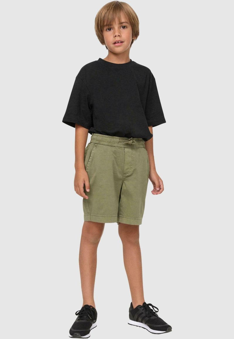 T-shirt en coton noir associé à un short vert kaki avec une taille élastique, terminé par des baskets de sport noires.
