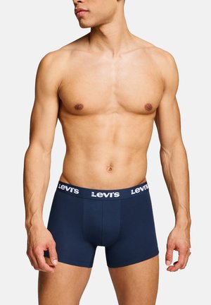 Shirtless man wearing navy blue Levi's boxer briefs with branded waistband, standing against a plain light background.
