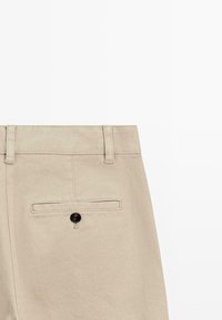 Pantalons en denim beige à coupe droite, dotés d'une poche arrière avec bouton et passants de ceinture. Coutures visibles le long des bords.