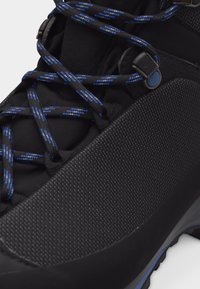 Μαύρο ορειβατικό μποτάκι με υφή πλαϊνής επιφάνειας, στρογγυλά κορδόνια σε μαύρο και μπλε μοτίβο και μεταλλικά οφθαλμοί για τα κορδόνια.