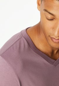 V-neck purple t-shirt with a smooth texture. Fabric appears lightweight with a fitted design and subtle stitching detail on the shoulder.